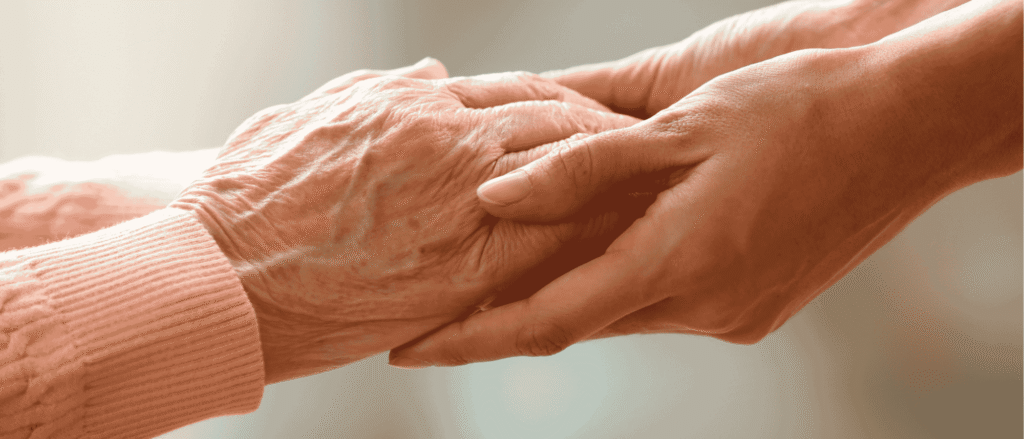 An adult child gently holding an elderly parent's hands, representing care in the inheritance conversation