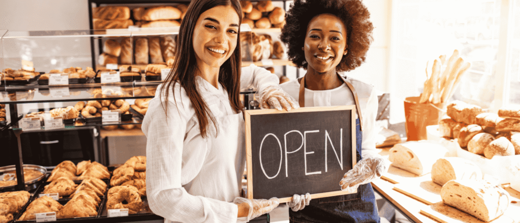 Two smiling bakery owners holding an Open sign, the kind of family business a business continuity plan helps keep open