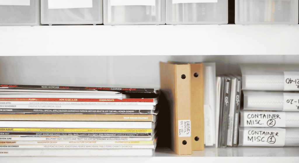 Binders, magazines and labeled storage boxes on a white shelf, a reminder to keep estate documents and trust funding organized