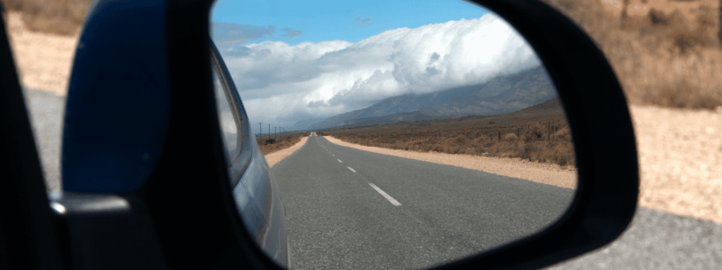 A car's side mirror reflecting the road behind, a reminder that recency bias in investing looks backward