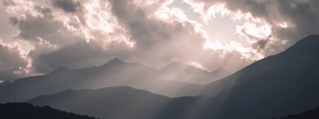 Sunlight breaking through storm clouds over a mountain range, a reminder that market downturns pass