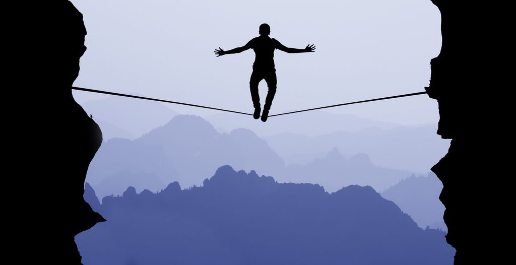 Person balancing on a tightrope between cliffs, illustrating the tug of war between headlines and fundamentals