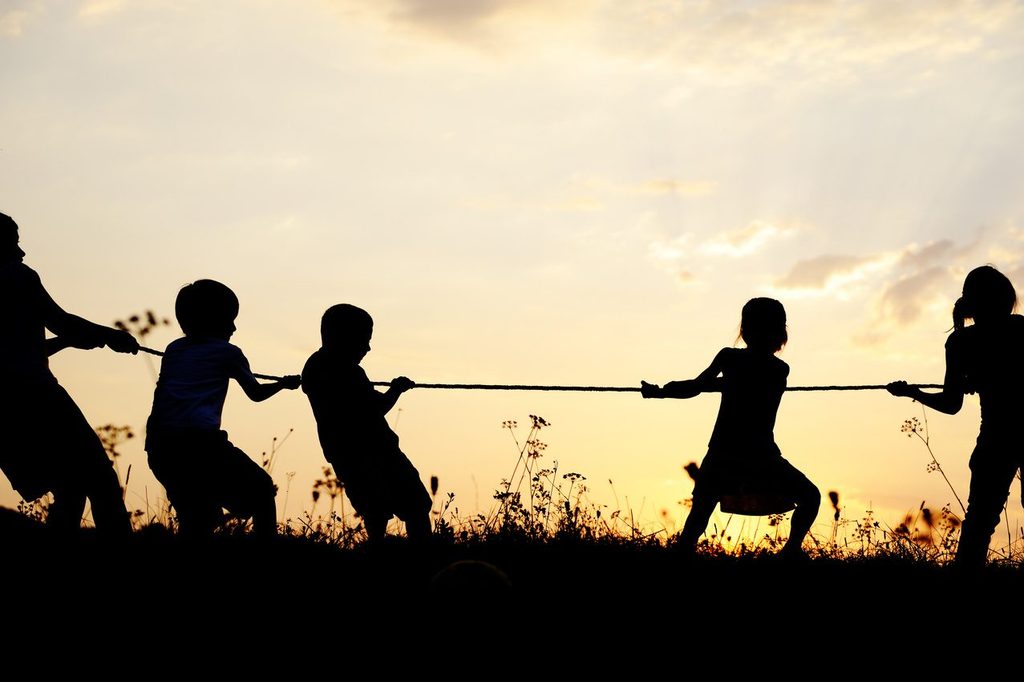 Silhouettes playing tug of war at sunset, illustrating the economy's pull between growth and inflation